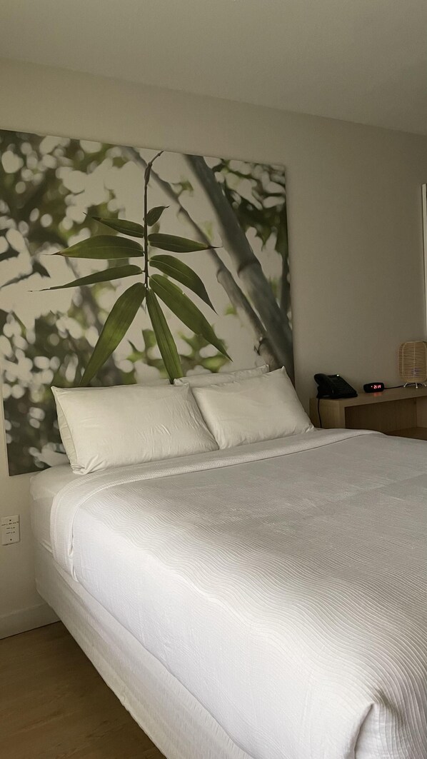 Una cama bien tendida con sábanas blancas, un teléfono montado en la pared y un reloj digital que marca las 2:11.