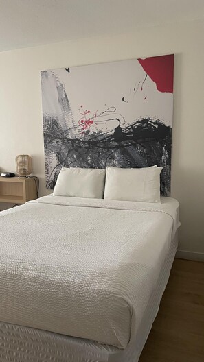Un dormitorio con una cama grande, una mesita de noche y una obra de arte en la pared.