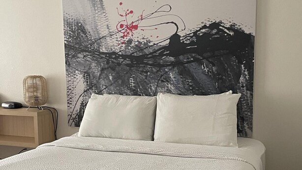 Ein Schlafzimmer mit einem großen Bett, einem Nachttisch, einer Lampe und einem Wandbild.
