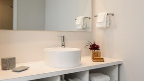 Ein modernes Badezimmer mit einem weißen Waschbecken, einem großen Spiegel und einer Holzvase mit Blumen.