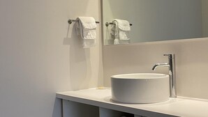 Ein modernes Badezimmer mit einem weißen Waschtisch, einem großen Spiegel und integrierten Ablagen für Handtücher.