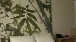 Ein ordentlich bezogenes Bett mit weißer Bettwäsche, ein an der Wand montiertes Telefon und eine Uhr, die 2:11 Uhr anzeigt.