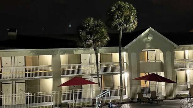 A hotel with a swimming pool, outdoor seating, and palm trees.