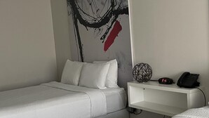 A modern hotel room with a bed, a bedside table with a phone and a clock, and a wall with abstract art.