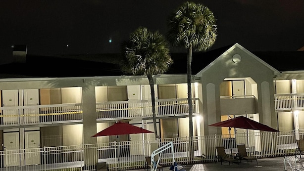 A hotel with a swimming pool, outdoor seating, and palm trees. - Deluxe Apartment Two Queen (Kissimmee)