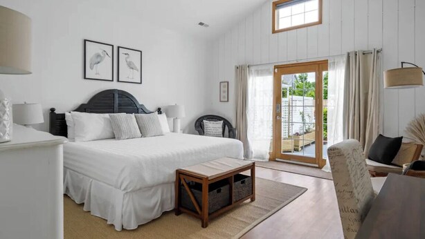 A bedroom with a bed, bedside tables, a chair, a window, and a door leading to a balcony.