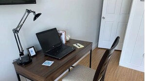 A wooden desk with a laptop, a desk lamp, a chair, and a small framed picture.
