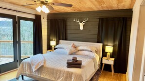 A bedroom with a bed, two bedside lamps, a ceiling fan, a deer head decoration, and a view through a window. - Sunset Mtn View*Pool*Hot Tub*Massage Chair*Theater Rm*Pickleball*Game Rm*Hiking (Mars Hill)