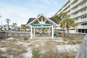 Relax on the covered patio with a stunning beach view, featuring a flat roof, two benches, and a table.