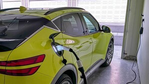 Ein gelber Wagen steht in einer Garage, an der eine Ladestation angebracht ist.