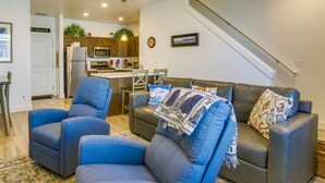 Ein modernes Wohnzimmer mit einer Couch, zwei Sesseln, einem Essbereich mit Tisch und Stühlen, einer Küche mit Geräten und einer Treppe.
