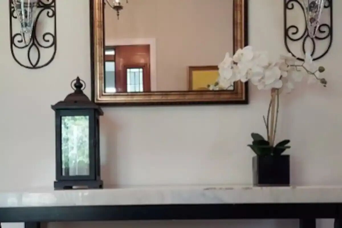 A wall-mounted mirror with a decorative frame, a black lantern, and a potted plant with white flowers.