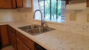 A kitchen with a double stainless steel sink, wooden cabinets, and a window with a view of trees.