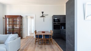 Ein Essbereich mit Holztisch und Stühlen, einer Vitrine und einer Küchenzeile mit Mikrowelle und Backofen.