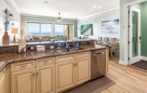 A kitchen with a large island, a dining area with chairs, and a view of the ocean through large windows.
