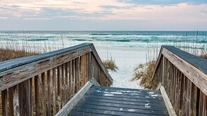 Une promenade en bois menant à une plage où l’on peut voir des vagues.