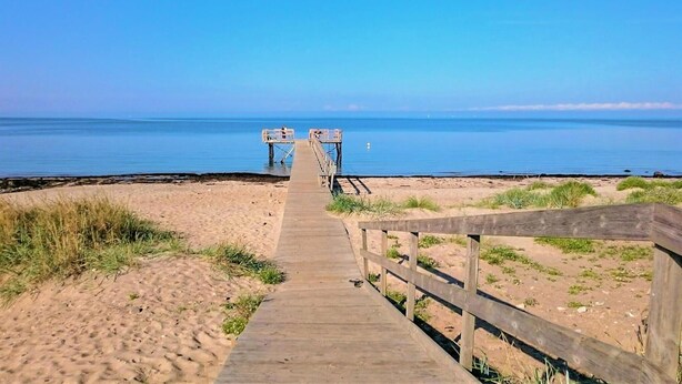 Une promenade en bois qui mène à une jetée s’avançant dans la mer.