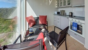 Un balcon avec une table et des chaises, une cuisine avec des meubles blancs et une vue sur l’extérieur.