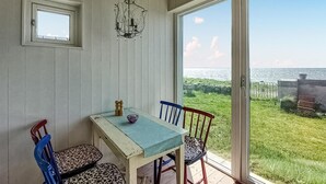 Un coin repas avec une table et des chaises, un lustre et une vue sur la mer par une porte vitrée.