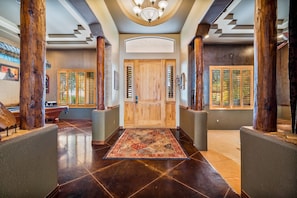 Un vaste hall d’entrée doté d’une porte en bois, de grandes colonnes en bois et d’un tapis à motifs.