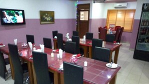 A dining area with multiple tables and chairs, a television mounted on the wall, and a refrigerator in the background. - Westine Hotels and Spa (Lekki)