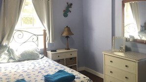 A bedroom with a bed, a nightstand, a dresser, a ceiling fan, and a window with curtains.