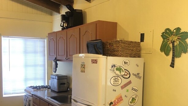 A compact kitchen with wooden cabinets, a white refrigerator, and a window with blinds.