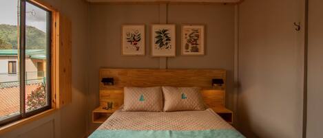A bedroom with a wooden headboard, a bed with a quilted cover, and three framed botanical prints on the wall.