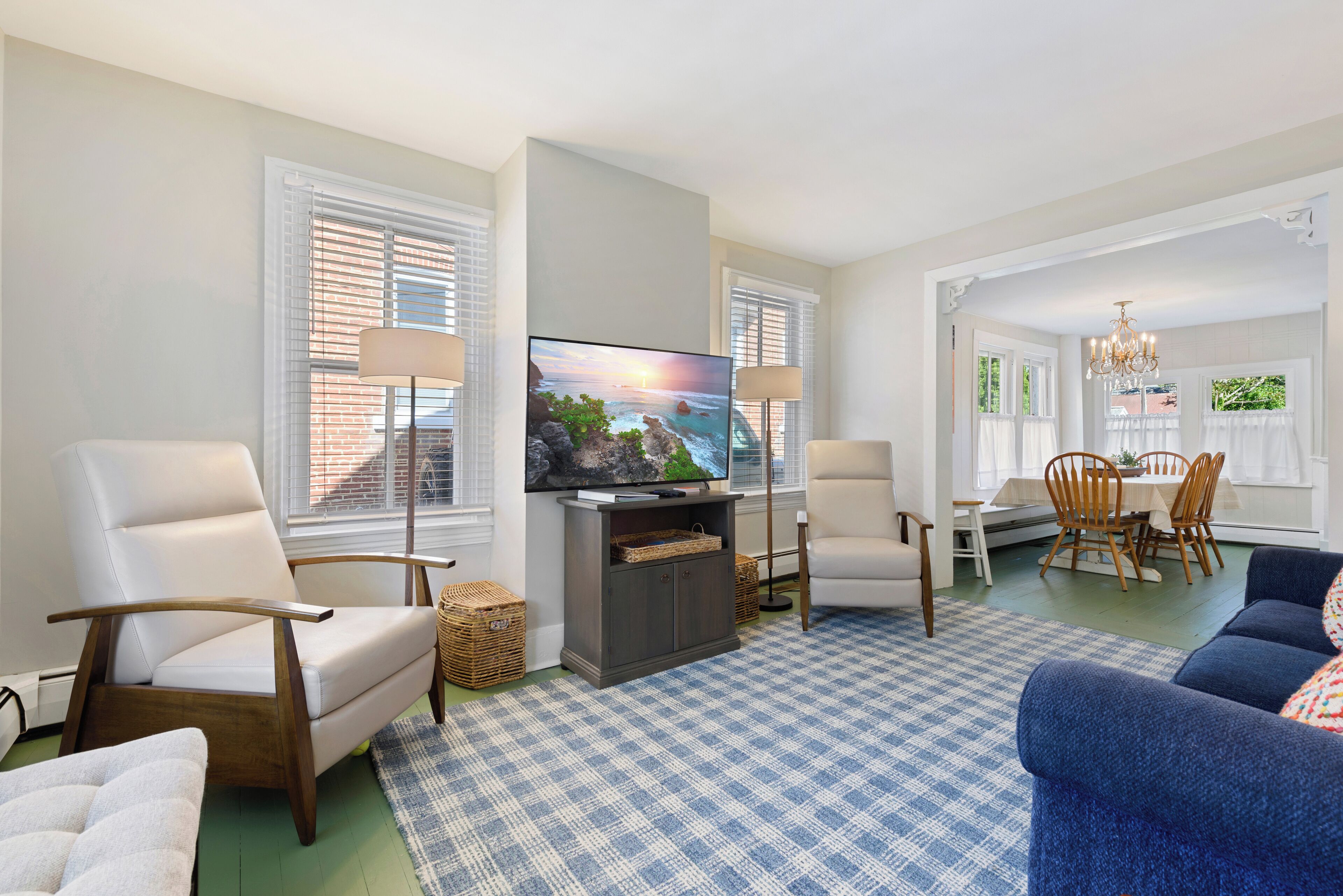 A living room with a television, two armchairs, a sofa, a dining table with chairs, and a chandelier.
