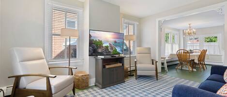 A living room with a television, two armchairs, a sofa, a dining table with chairs, and a chandelier.