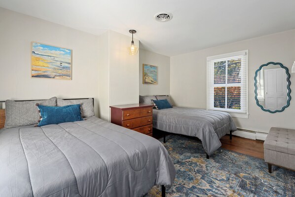 A bedroom with two beds, a dresser, a window with blinds, and a decorative mirror.