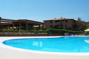 A swimming pool with a covered area, a building with a flat roof, and a clear sky.