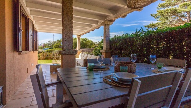 Une terrasse extérieure avec une table dressée pour le repas, des piliers en pierre et une vue sur le jardin.