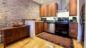 Een keuken met houten kastjes, een bakstenen muur, een vaatwasser en een fornuis.
