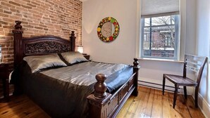 Een slaapkamer met een bakstenen muur, een houten bed, een raam met zonwering en een decoratieve ronde wandversiering.