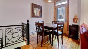 Een eethoek met een houten tafel en stoelen, een hanglamp, een spiegel en een Boeddhabeeld.