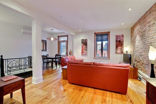 Una sala moderna con un sofá rojo, suelo de madera y una pared de ladrillo decorativa.
