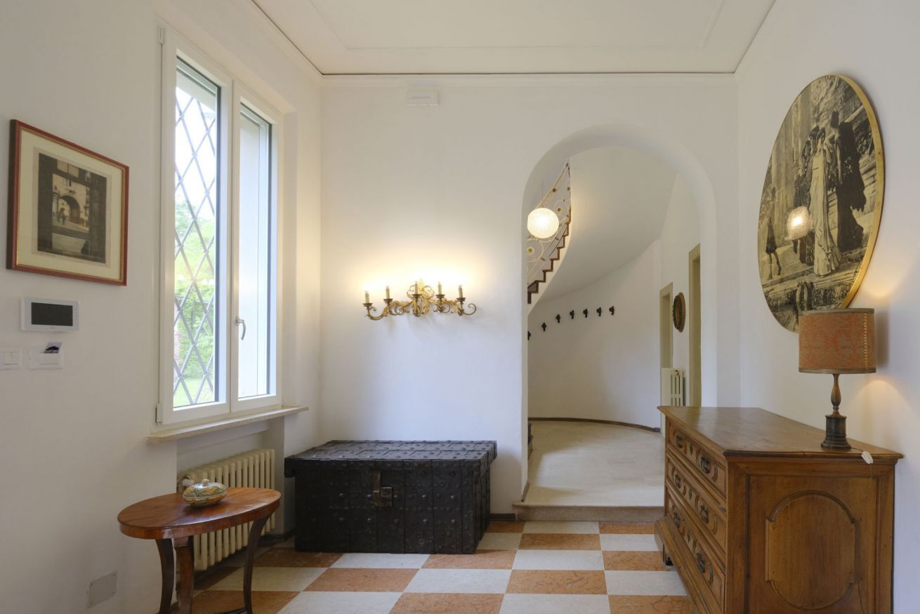 Un couloir avec un sol à carreaux, un escalier, un radiateur, un tableau encadré, un luminaire fixé au mur et un meuble en bois.