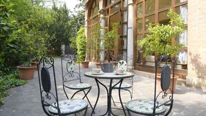 A patio with a round table and four chairs, surrounded by potted plants and a building with large windows. - GuestHost - Stunning villa divided over three levels (ground, first and second), WITHOUT lift. There are internal stairs to access the upper floors.In 410 square meters of space it comfortably accommodates 12 people.Detached villa with a private garden s (Ferrara)