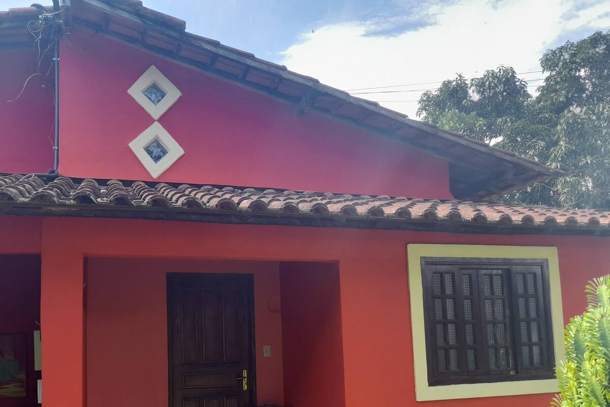 Um edifício vermelho com porta de madeira, uma janela com grades e uma pequena mesa do lado de fora.