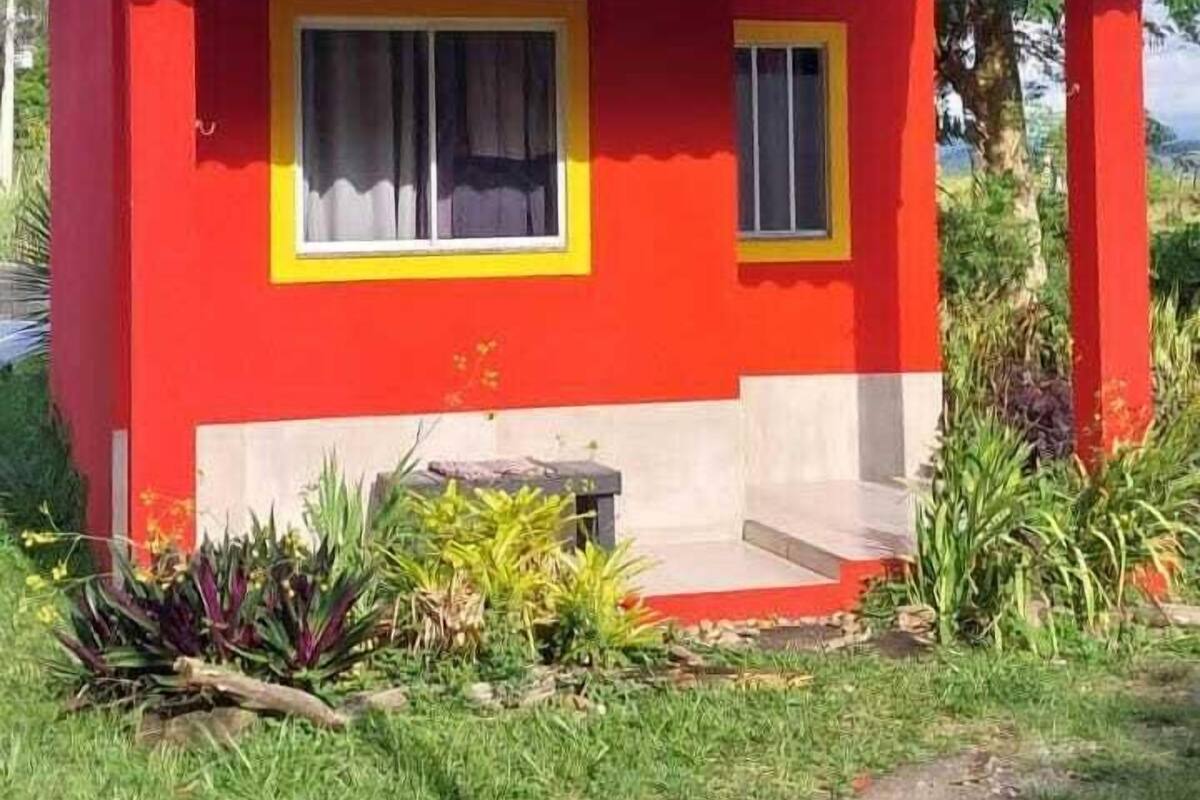 Uma casa vermelha com telhado de telhas, janela com detalhes em amarelo e uma pequena varanda.