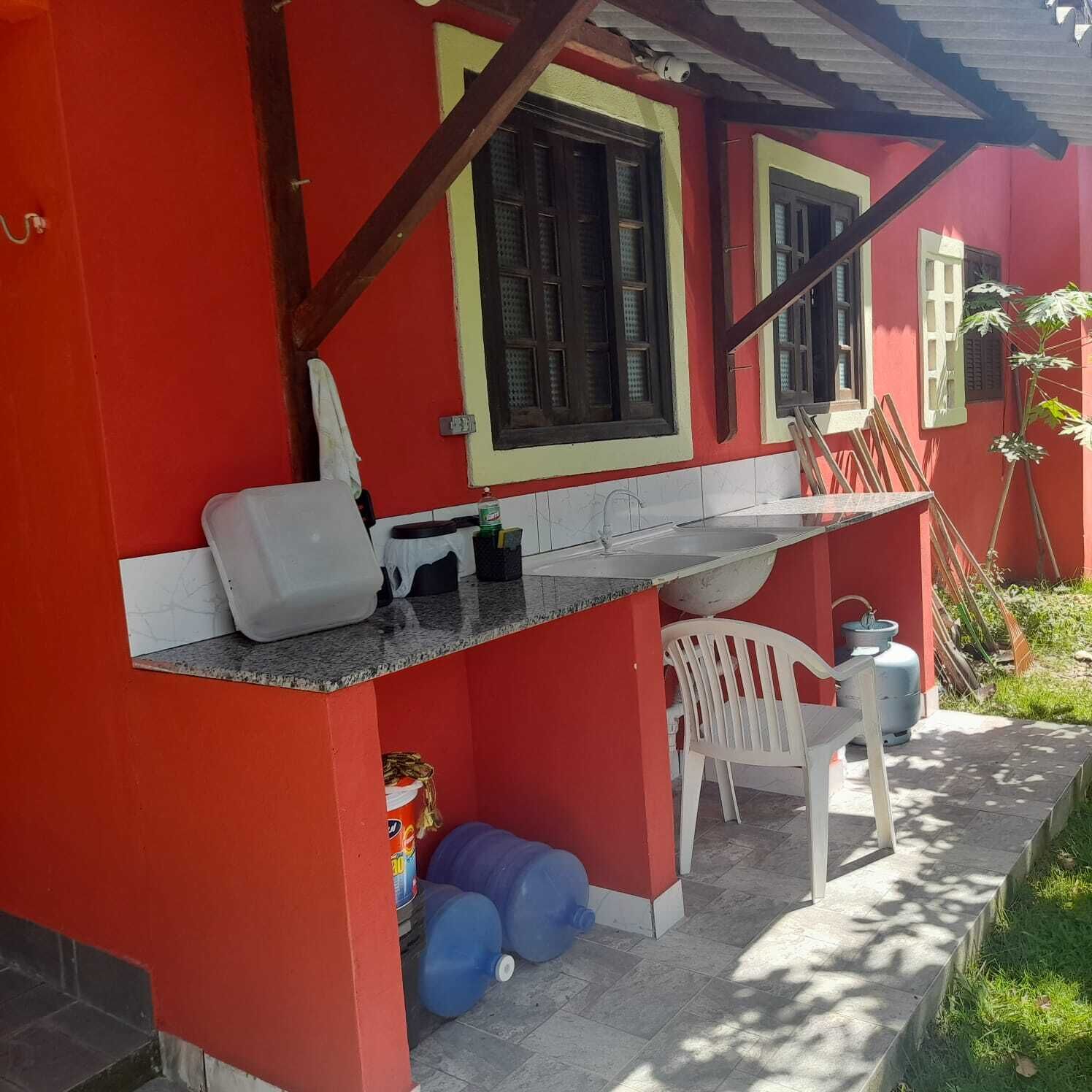 Un edificio rojo con un pequeño espacio al aire libre, una silla blanca y recipientes azules para agua.