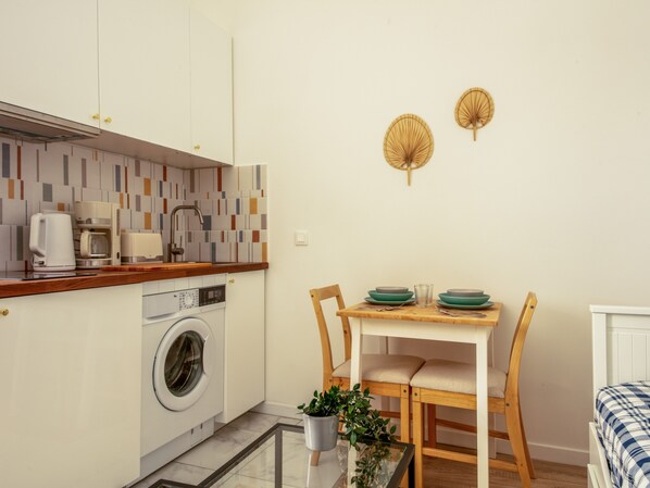 Een compacte keuken met een wasmachine, een koffiezetapparaat en een eethoek met een tafel en stoelen.