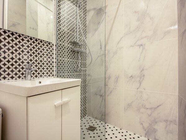 A bathroom with a white sink, a mirror, and a shower with a patterned wall.