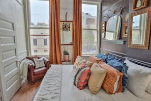 Ein Schlafzimmer mit Bett, Sofa, Vorhängen am Fenster und einem Spiegel an der Wand.
