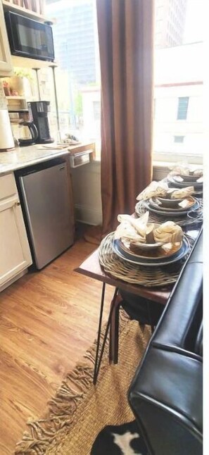 A compact kitchen with a dining area, a small refrigerator, a coffee maker, and a television on the wall.
