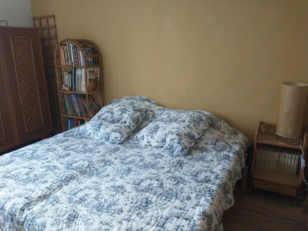 A bedroom with a bed covered in a patterned blanket, a wooden bookshelf, and a radiator.