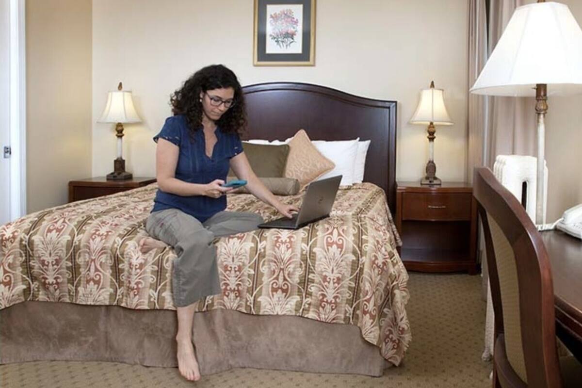 A hotel room with a bed, a laptop, and two bedside lamps.