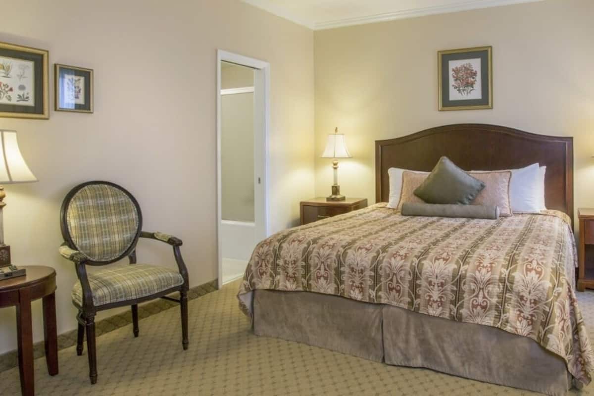 A hotel room with a large bed, two bedside tables with lamps, a chair, and framed pictures on the walls.