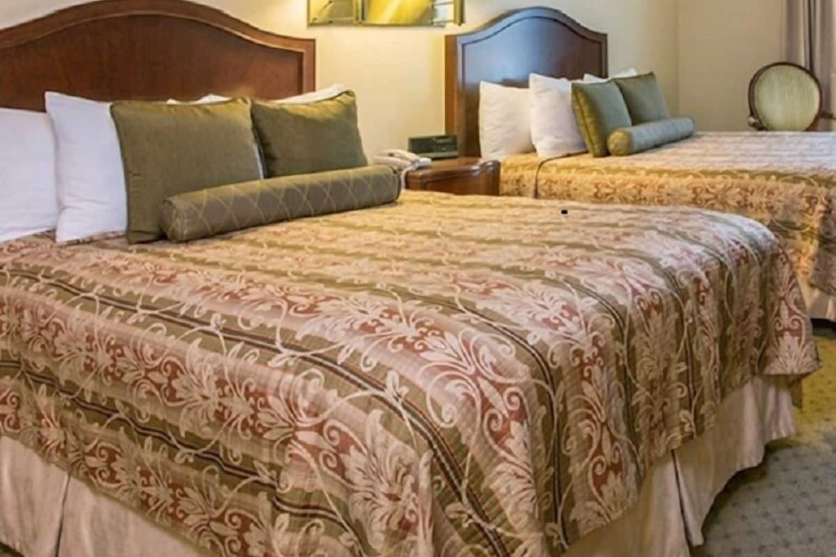 A hotel room with two beds, each with a wooden headboard, and a nightstand with a lamp between them.